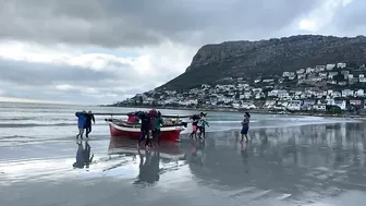 Cape Town Fishermen carrying row boat to shore at Fish Hoek beach